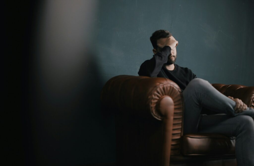 Mann sitzt nachdenklich auf einem Ledersessel und hält sich die Hand an die Stirn, als Ausdruck von emotionaler Belastung oder Nachdenklichkeit.