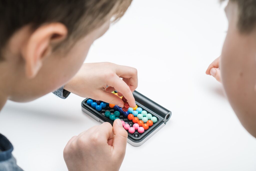 Zwei Kinder spielen mit einem farbenfrohen Denkspiel, bei dem bunte Kugeln in einem Logikspiel arrangiert werden.